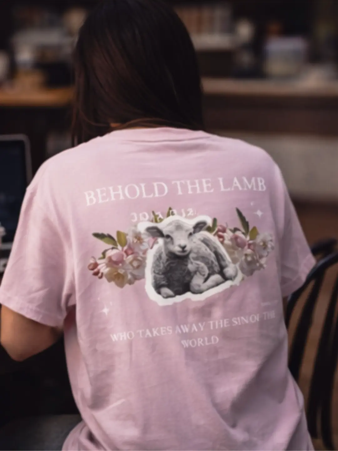 Back view of pink Christian T-shirt with lamb and floral design reading “Behold the Lamb – John 1:29”